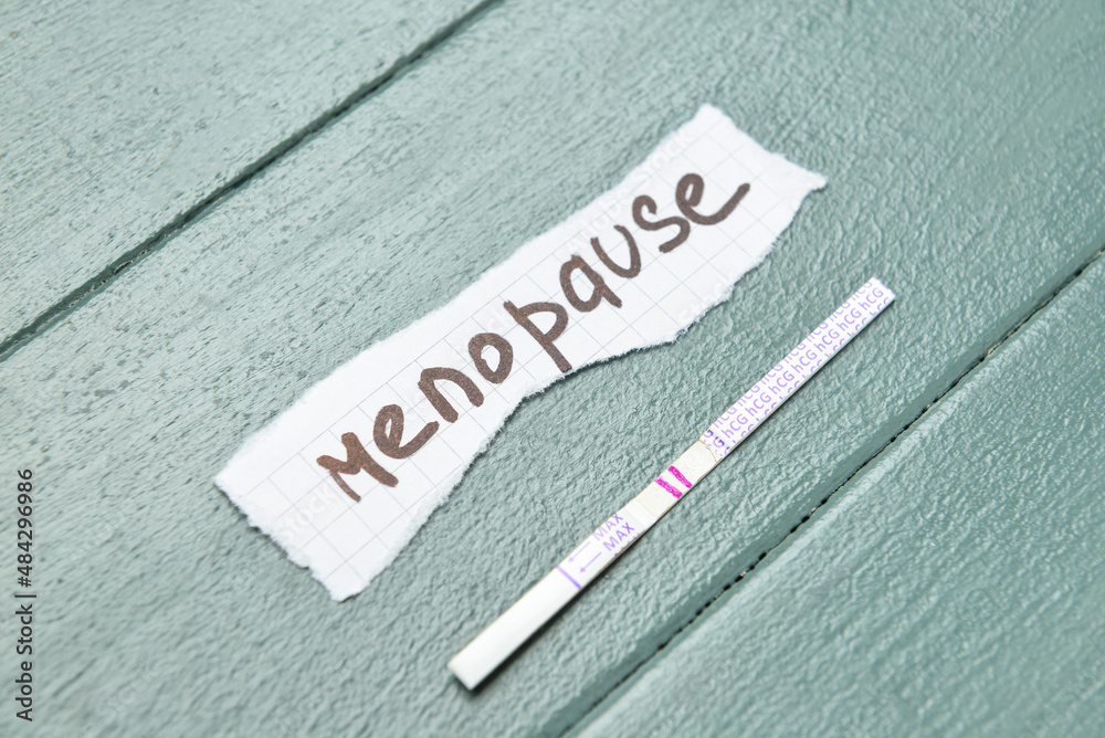 Paper piece with word MENOPAUSE and pregnancy test on color wooden background