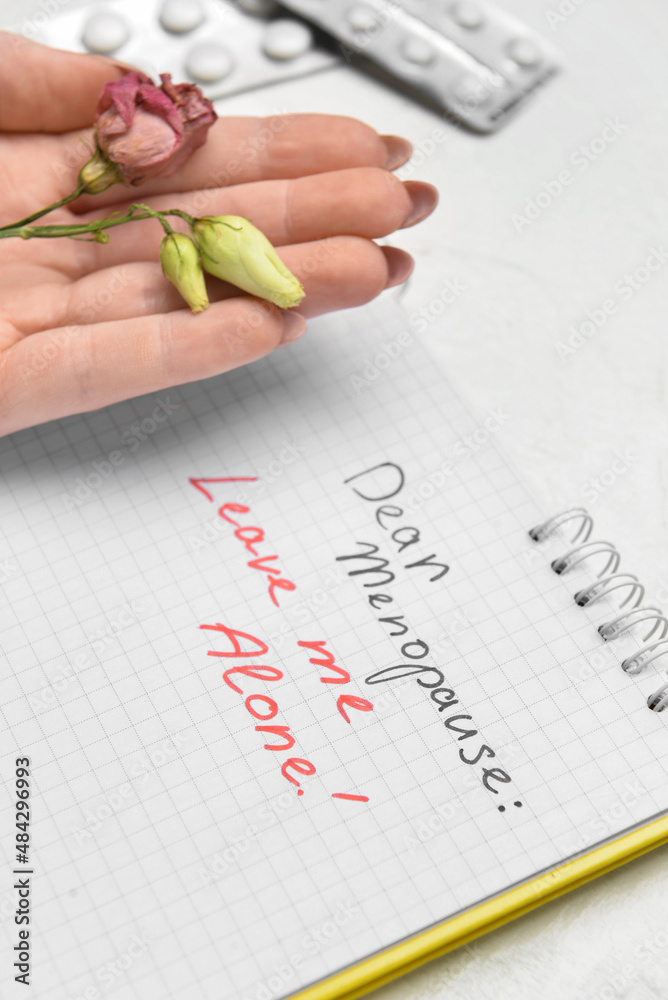 Notebook with text DEAR MENOPAUSE LEAVE ME ALONE, female hand, dried rose and pills on white backgro