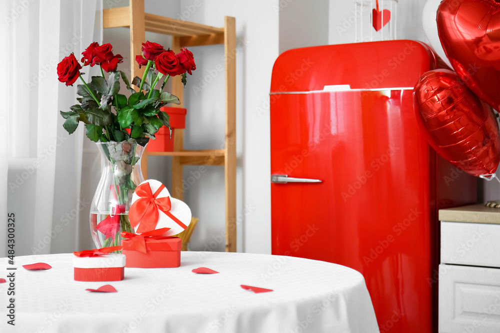 Gift boxes and vase with roses for Valentines Day celebration on dining table in light kitchen