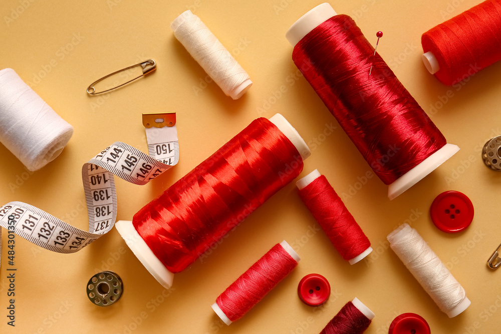 Thread spools, buttons and measuring tape on color background