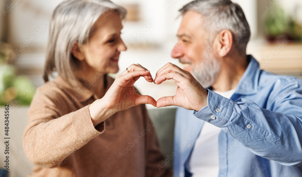 happy couple of elderly lovers shows a heart symbol with their hands, hugging on Valentines day