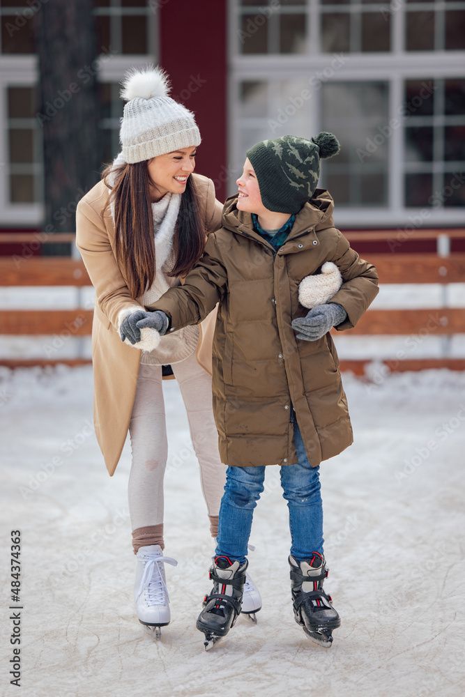 A child with his mom, learning how to ice skate. smiling and looking at each other.