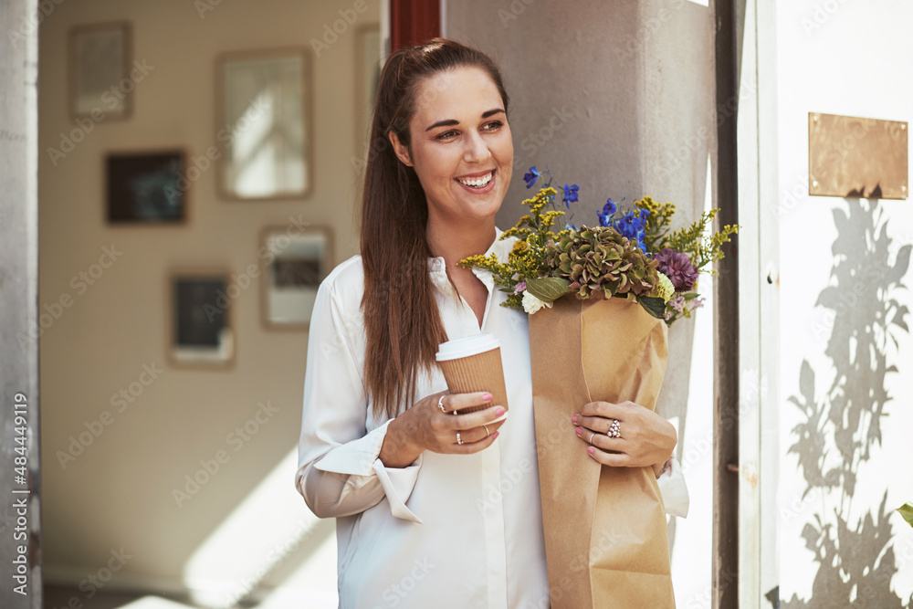 Smiling woman standing outside drinking a coffee and carrying flowers