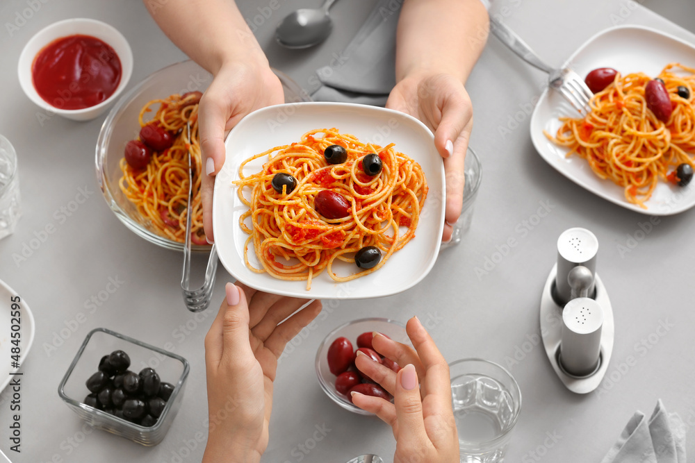 在餐厅的餐桌上，女人们端着一盘美味的Pasta Puttanesca