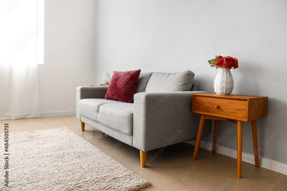 Stylish interior with wooden bedside table and couch near light grey wall