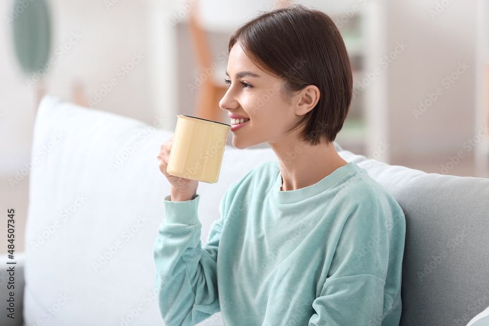 漂亮的年轻女人在家的沙发上喝着美味的茶