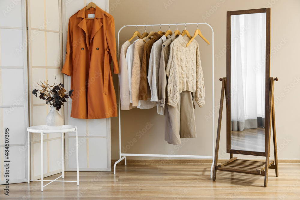 Rack with clothes and vase with autumn branches in room