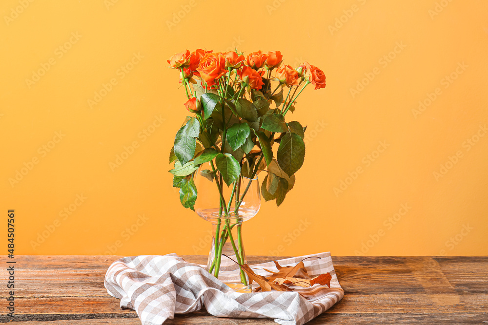 Vase with beautiful orange roses on wooden table against color wall