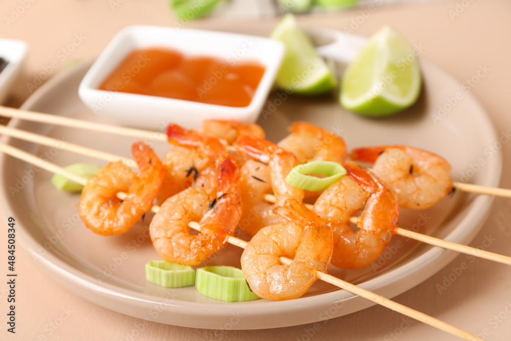 Plate with grilled shrimp skewers on beige background