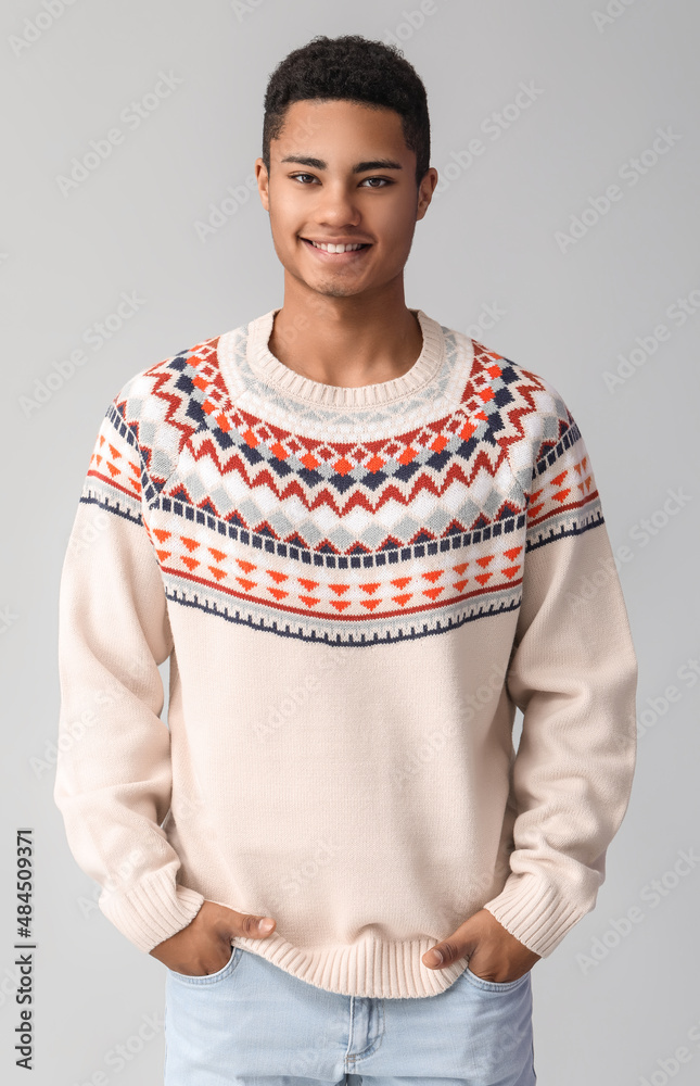 Handsome African-American guy in knitted sweater on light background