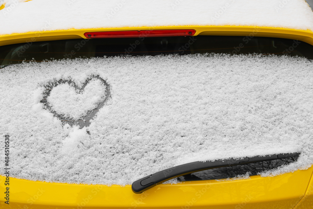 Heart drawn on snow covered car rear window on street, closeup