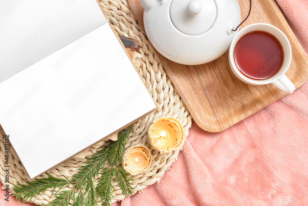 Opened book with blank pages, burning candles and tray with cup of tea on bed