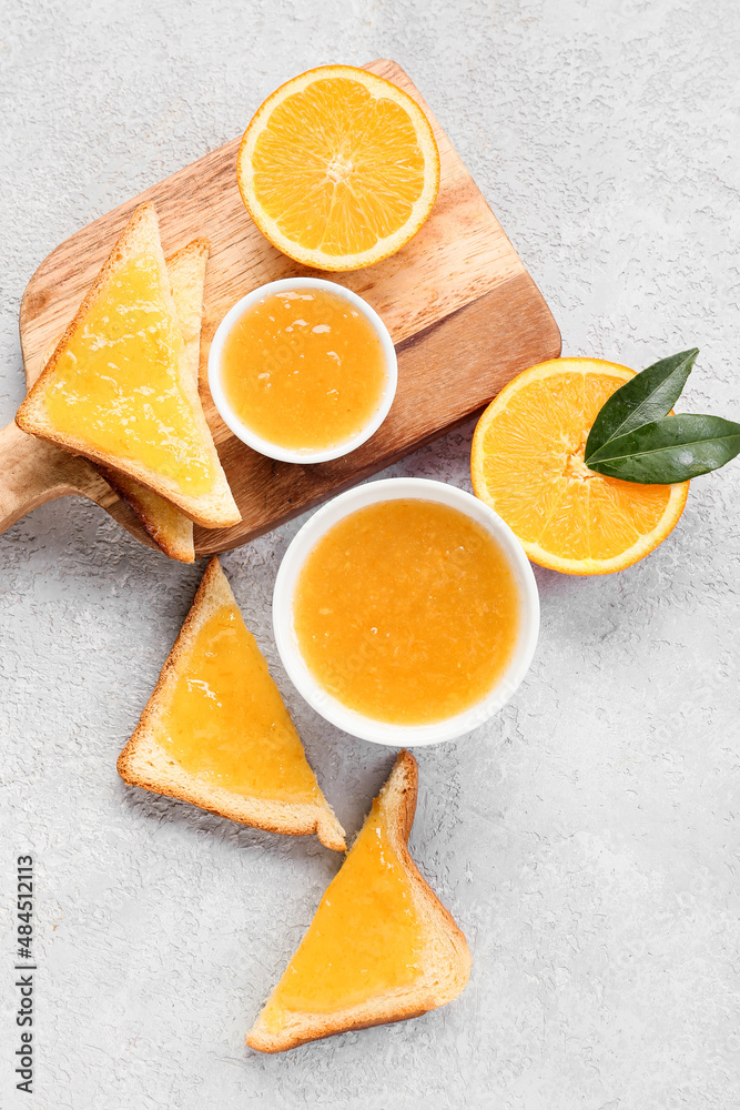 Bowls of tasty orange jam and toasts on light background