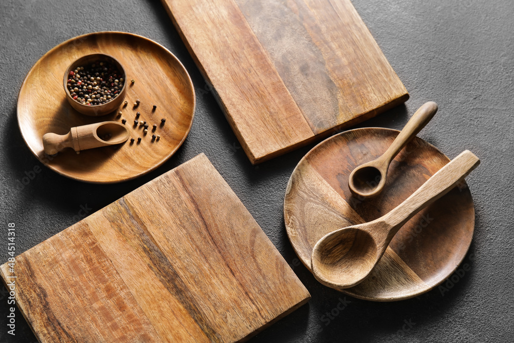 Wooden cutting boards, plates and spoons on black background