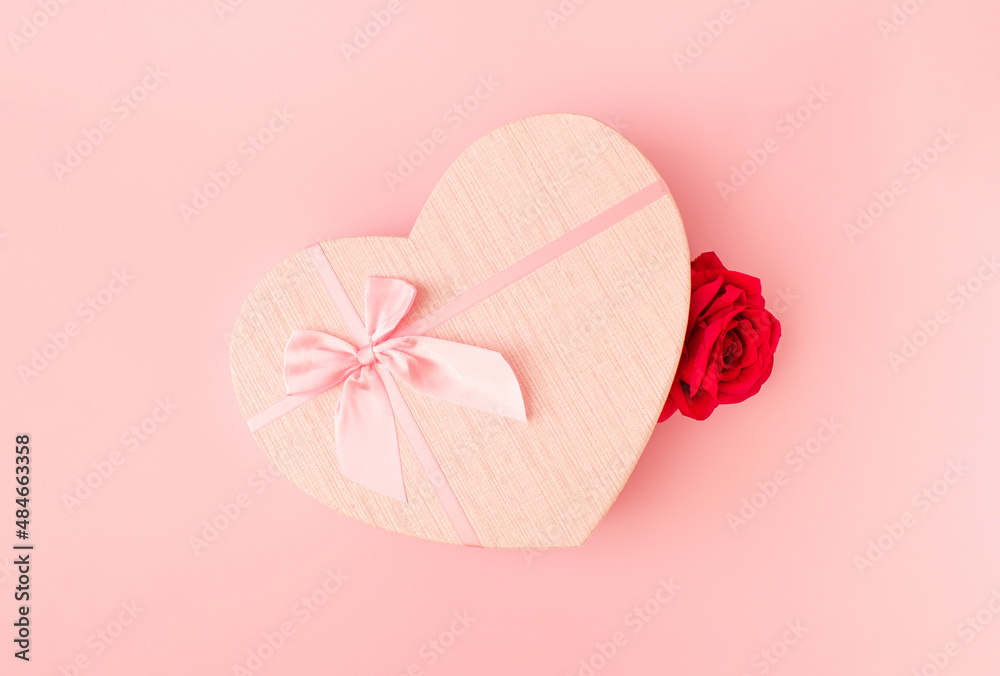 Creative idea made of heart shape gift box and red rose on bright pink pastel background. Minimal Va