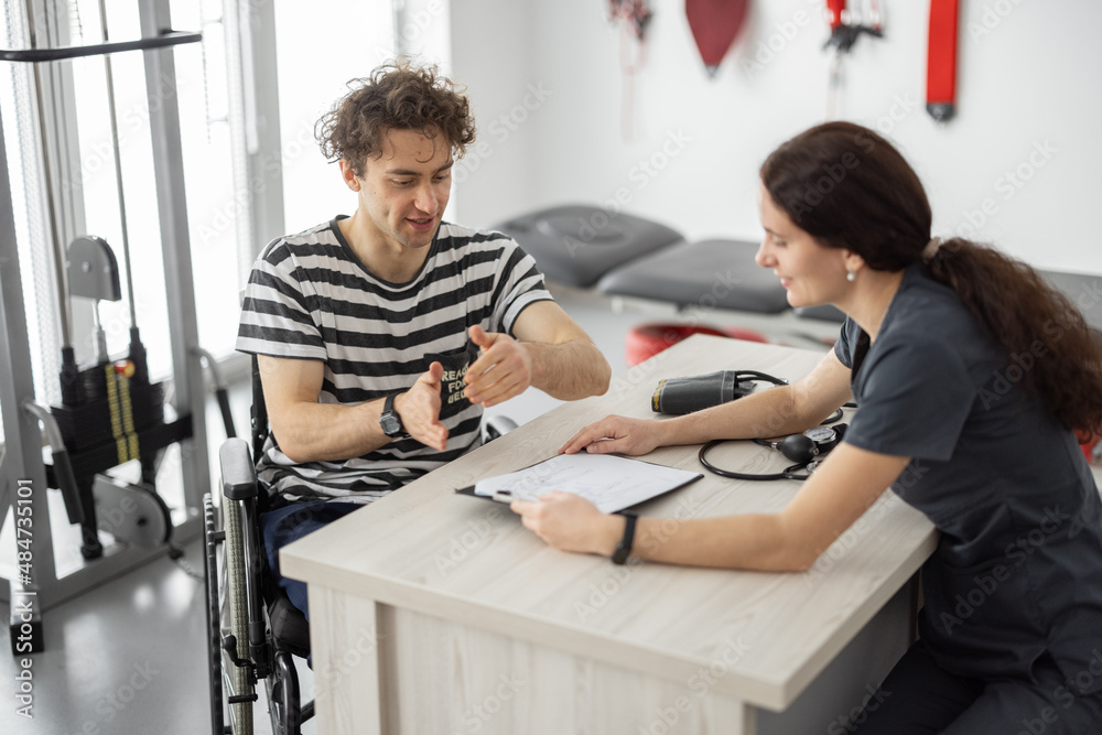 Medical worker talking with a young man in a wheelchair before training in the rehabilitation center