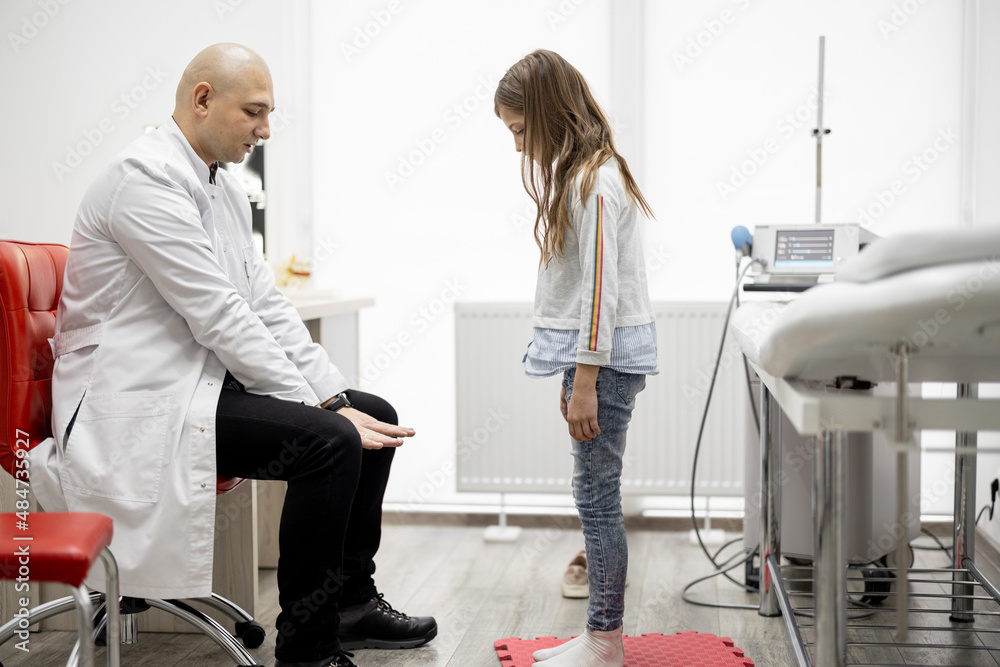 Physical therapist examines little girl in detail for musculoskeletal disorders in medical office. C