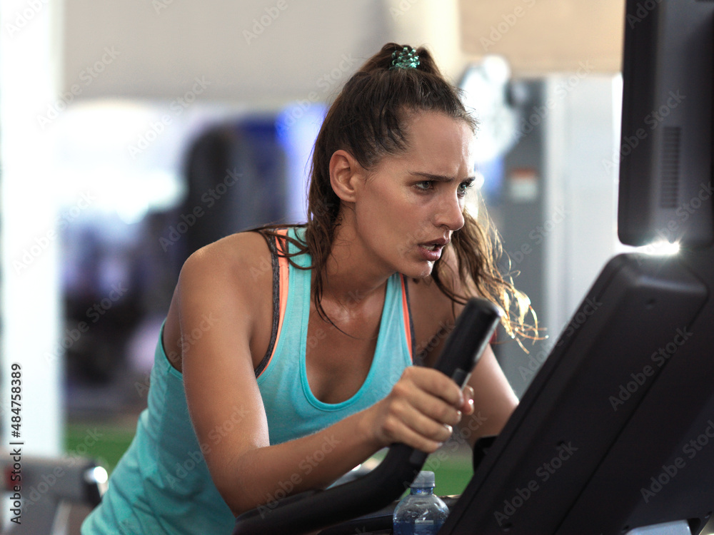 She just keeps on going. Shot of a determined looking young woman working out on an elliptical machi