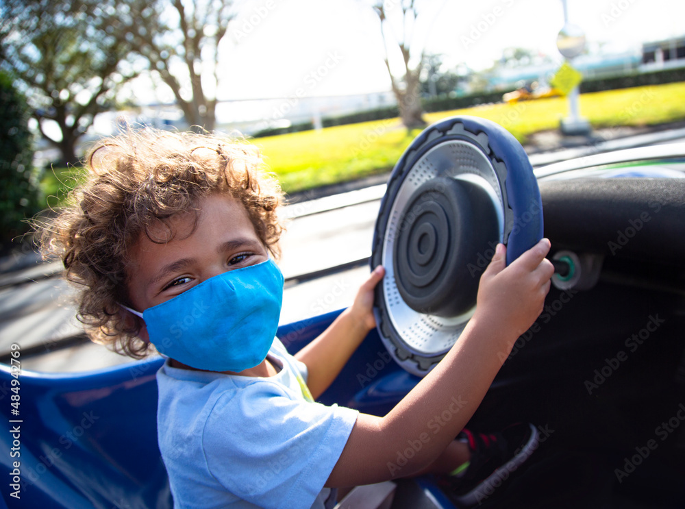 Cute African American child driving a fun go cart ride at an outdoor amusement park. He is wearing a