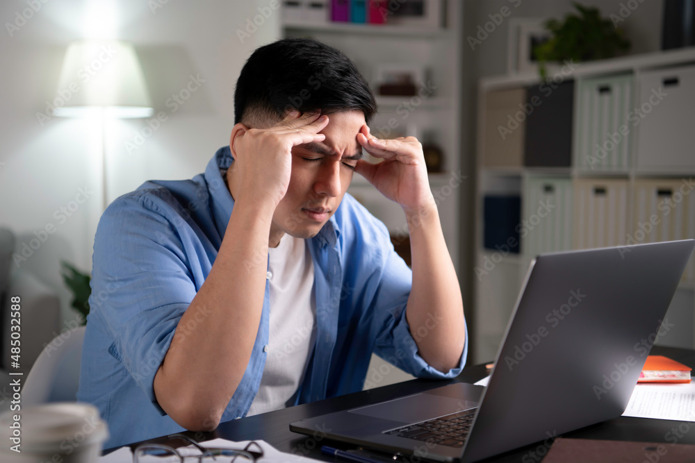 Young Asian businessman looking serious and stressed while using laptop to work from home.