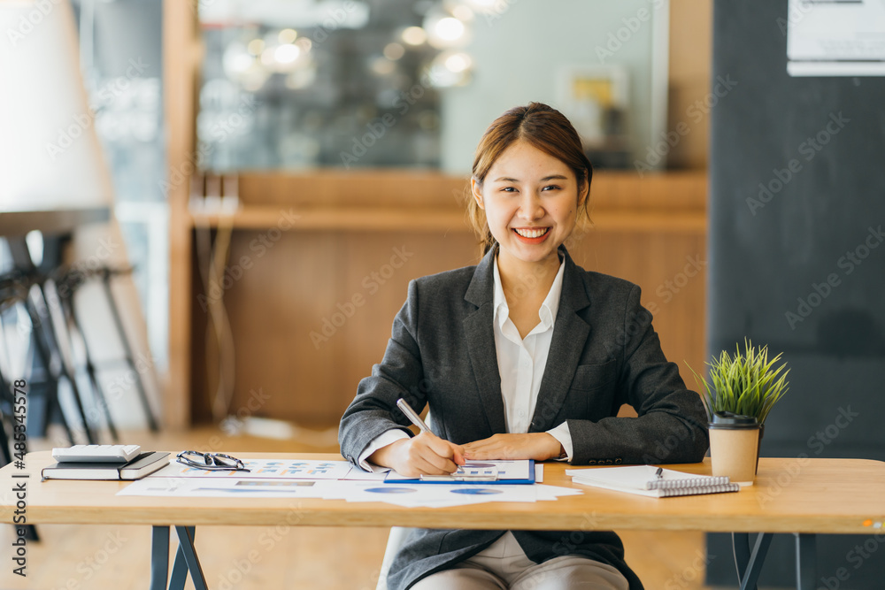 Confident young female financial advisor writing on diary while sitting with laptop at desk in offic