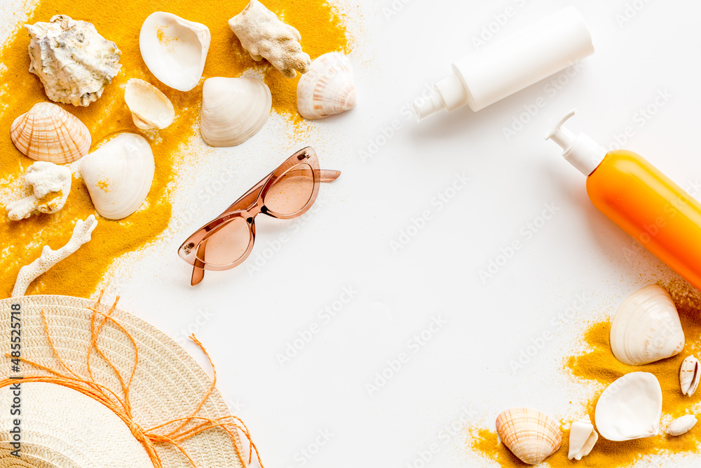 Beach sand and seashells with straw hat and bottles od sunscreen