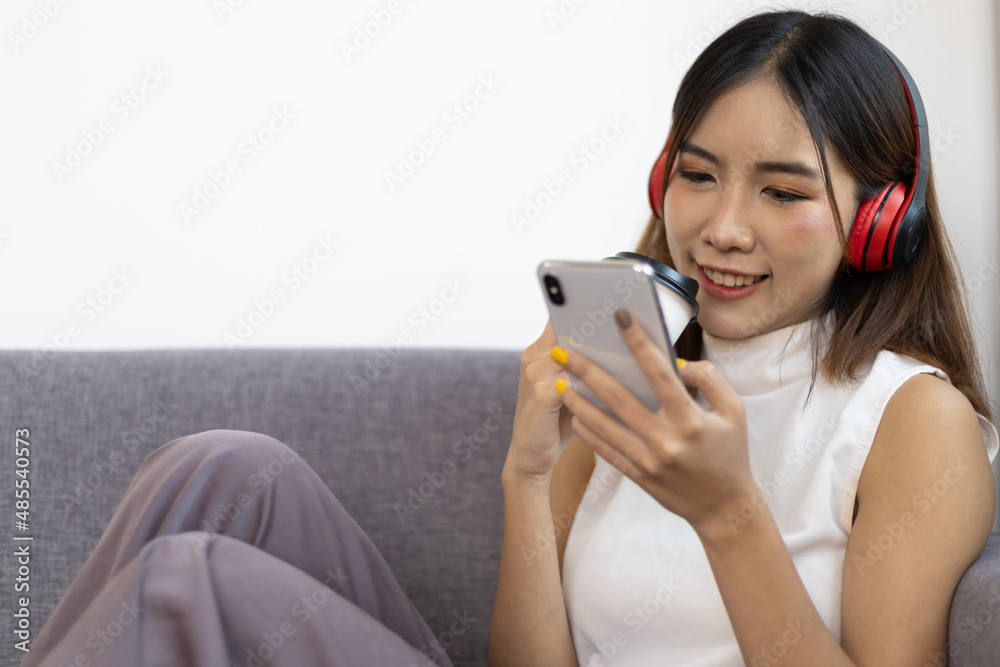 Close up lifestyle home life Asian woman sits using her mobile phone and listens to music on the sof