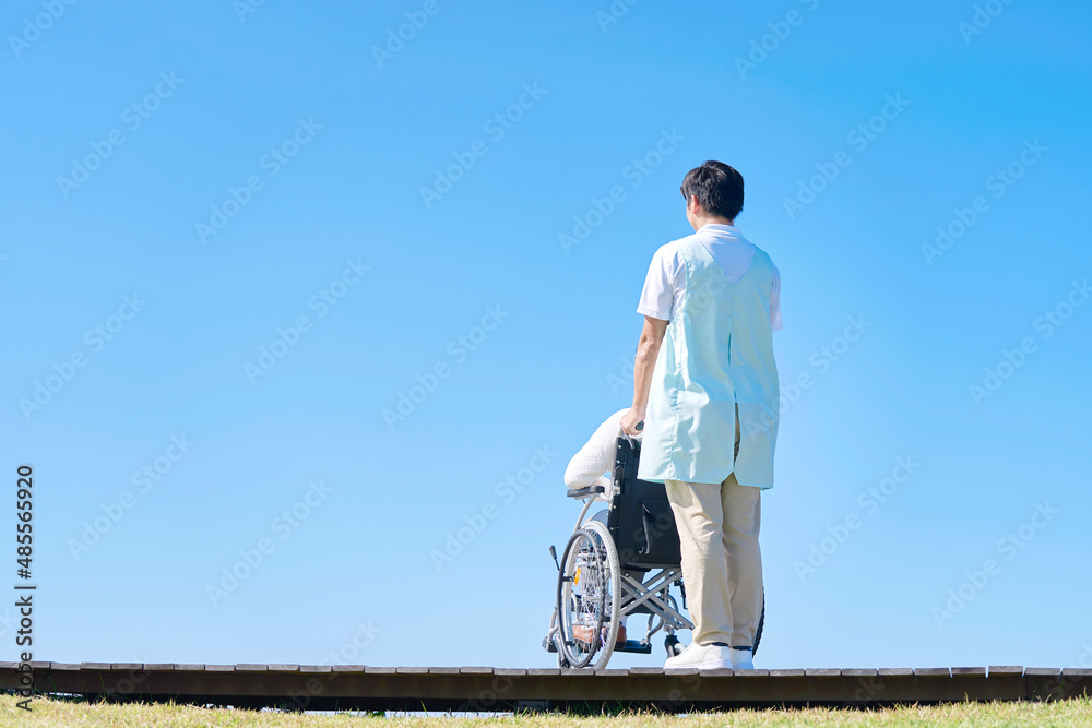 介護士と車椅子に乗る高齢者　屋外　後ろ姿