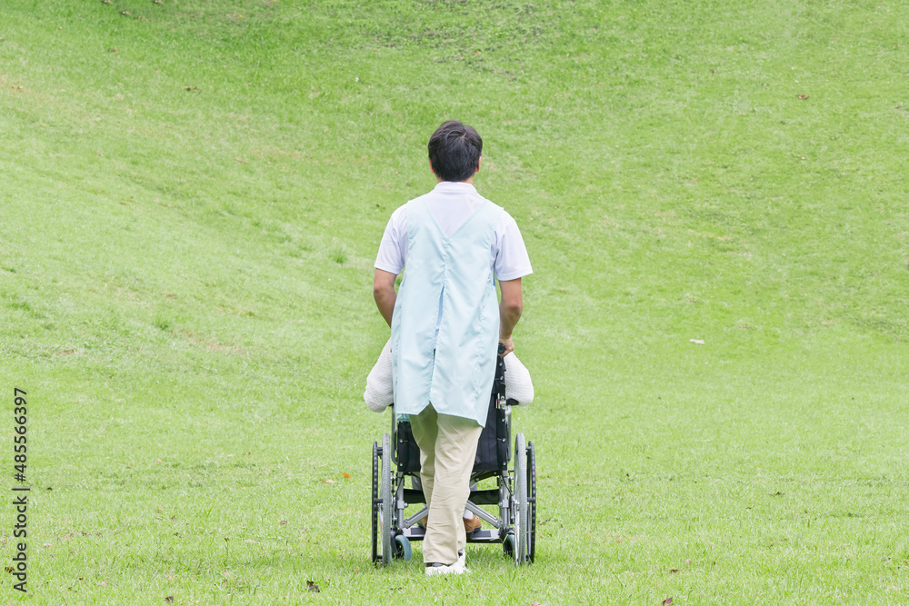 介護士と車椅子に乗る高齢者　屋外　後ろ姿