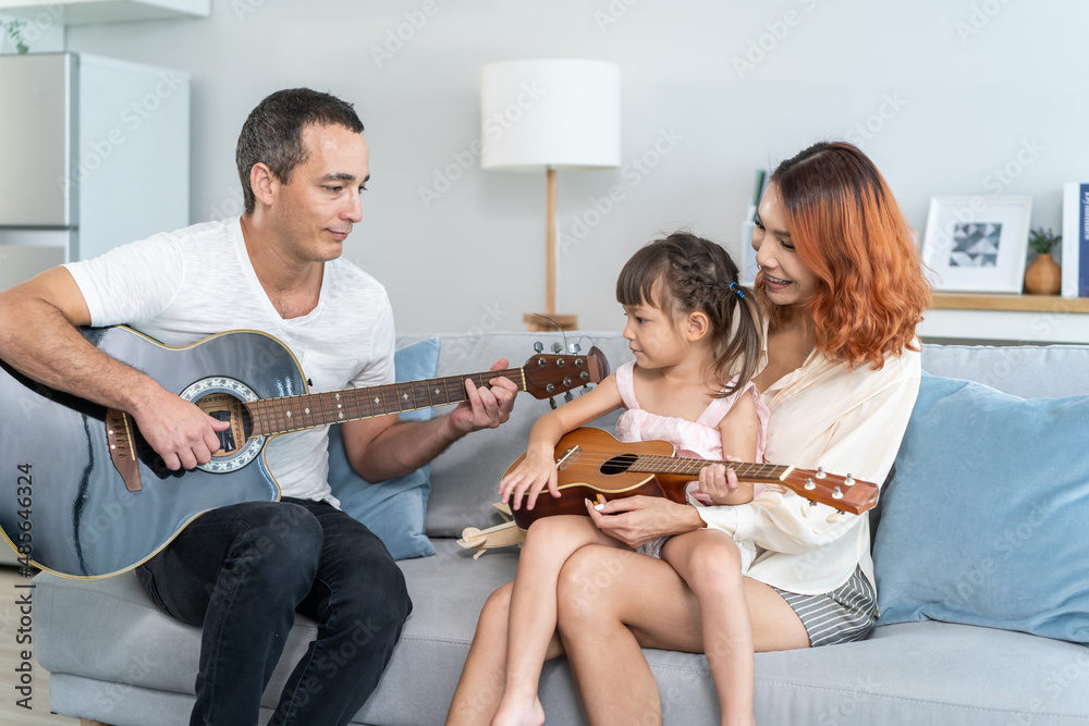 Asian young couple playing guitar with young baby kid together at home. 