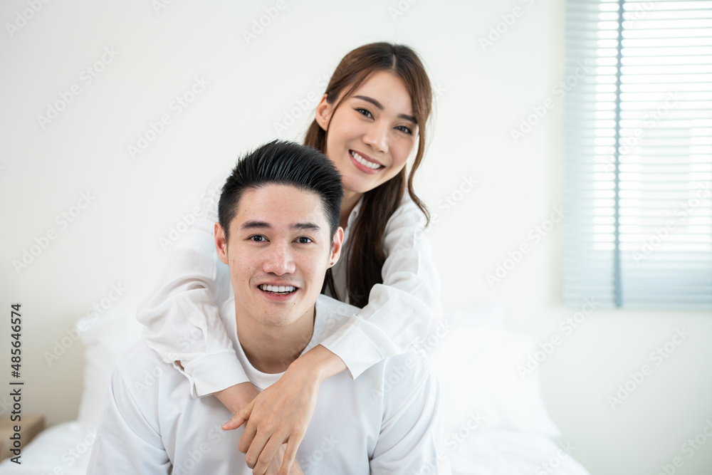 亚洲新婚夫妇坐在床上看着镜头的肖像。