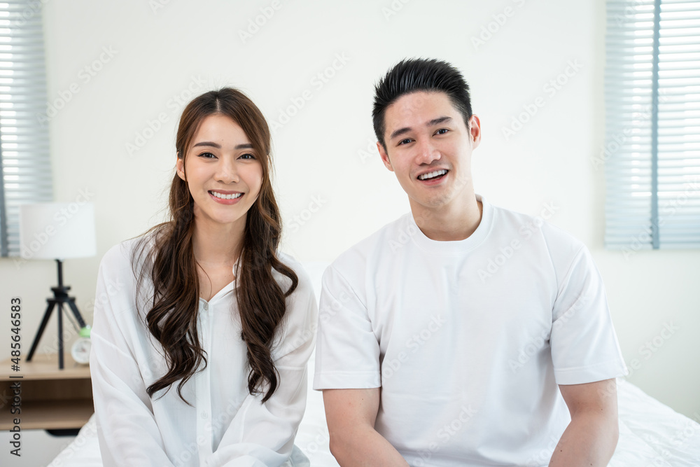 Portrait of Asian new marriage couple sit on bed and looking at camera. 