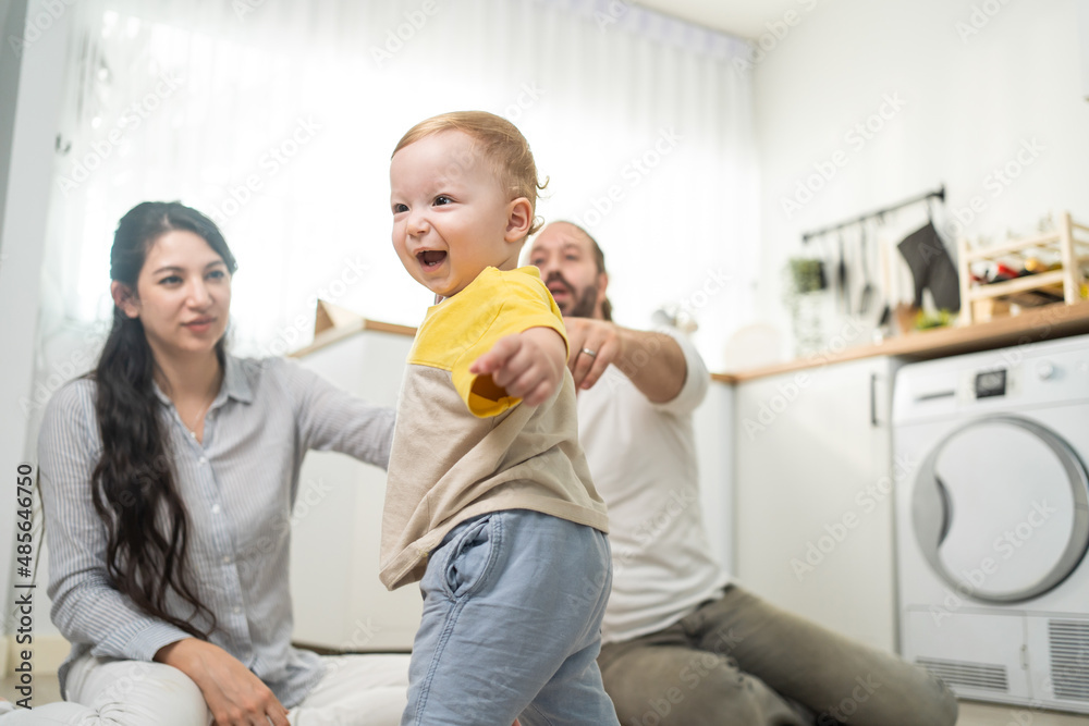 Caucasian baby boy child learn to walk with parents support in house. 