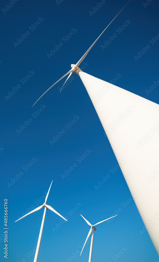 Wind farm with tree power generators against clear blue sky. Vertical shot, dramatic view from below