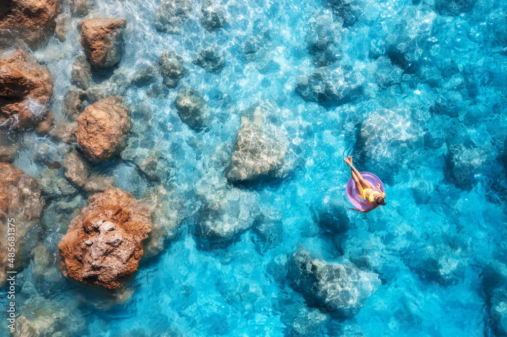 Aerial view of a young woman swimming with pink swim ring in blue sea at sunset in summer. Tropical 