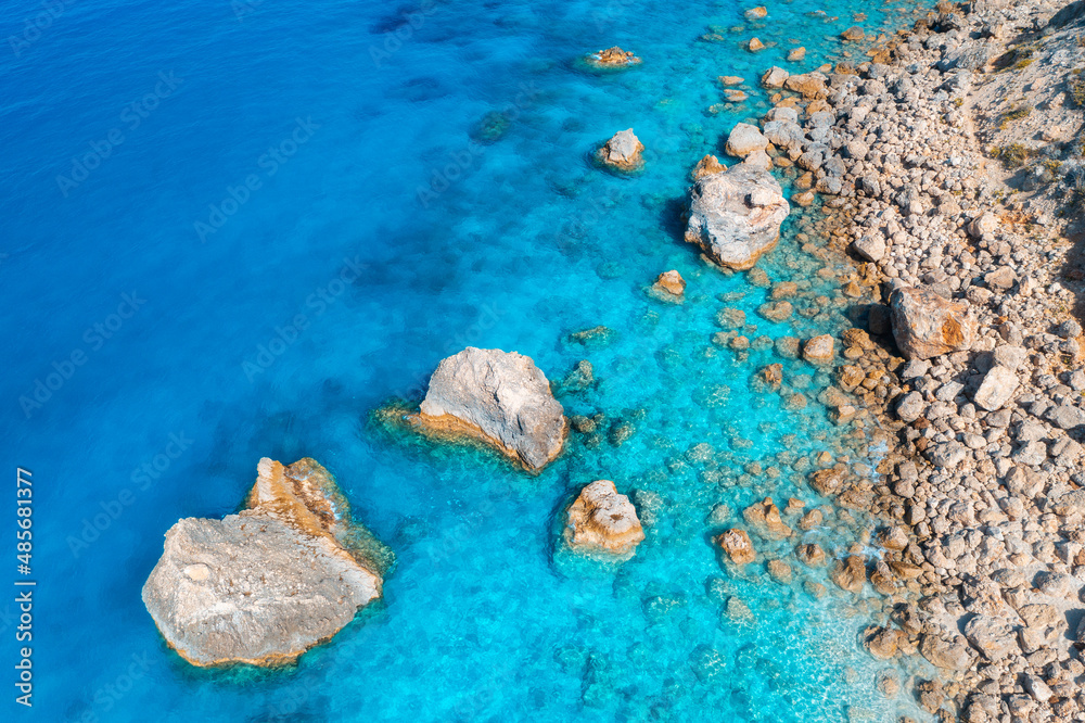 Aerial view of clear blue sea, stones and rocks in water, empty beach at sunset. Summer in Lefkada i