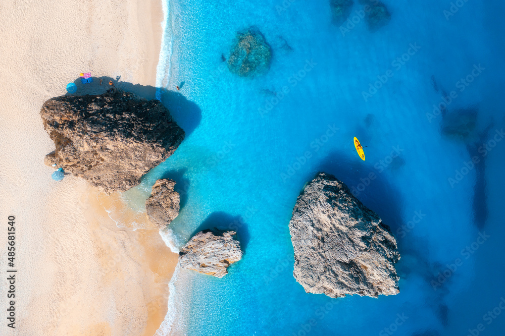 Aerial view of sandy beach, stones and yellow kayak in blue sea at sunset in summer. Canoe in clear 