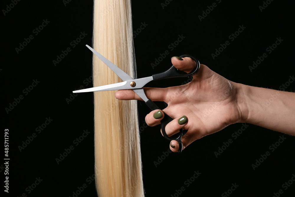 Woman cutting hair strand with scissors on dark background