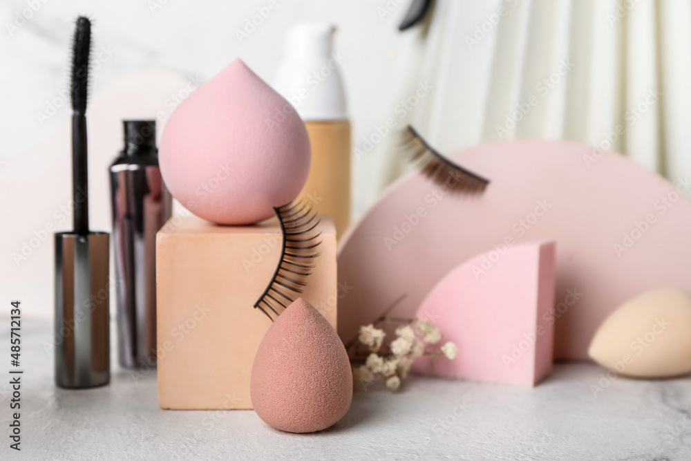 Different makeup sponges and cosmetics on light background, closeup