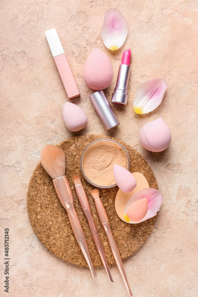 Composition with makeup sponges, brushes, cosmetics and petals on color background