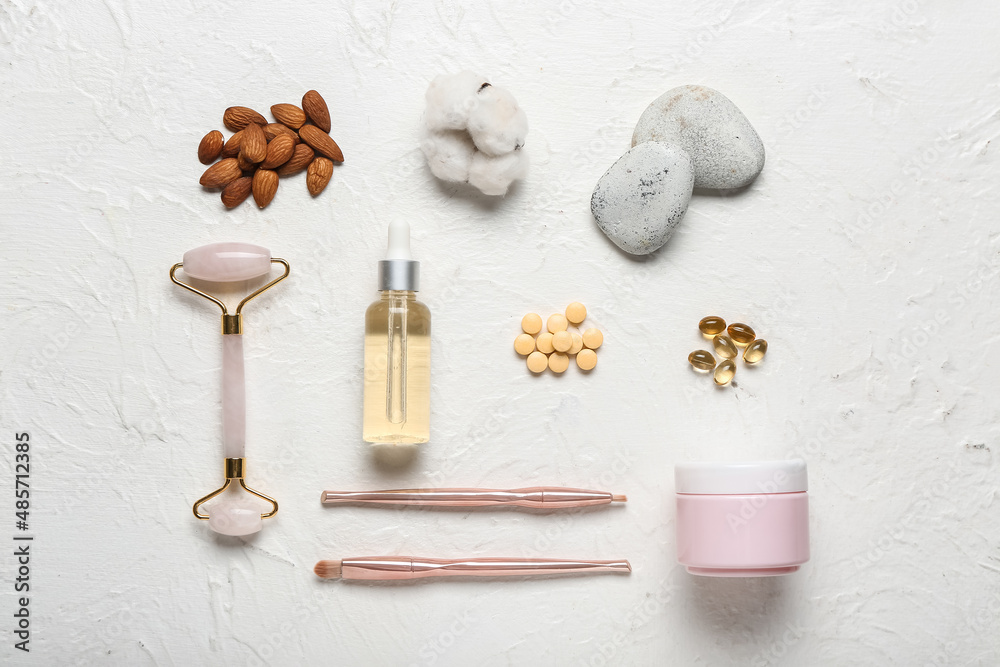 Composition with bottle of essential oil, pills, makeup supplies, jar of cream and almond nuts on li