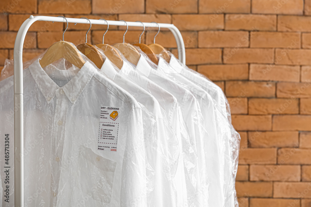 Rack with clean shirts in plastic bags near brick wall