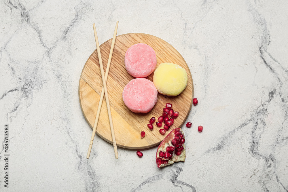 Board with delicious mochi, pomegranate and chopsticks on light background