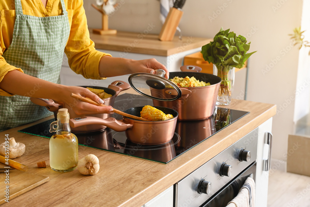 Woman in apron preparing corn cobs in kitchen