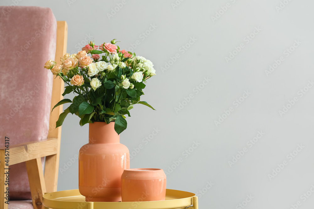 Vase with bouquet of beautiful fresh roses and candle on table near white wall