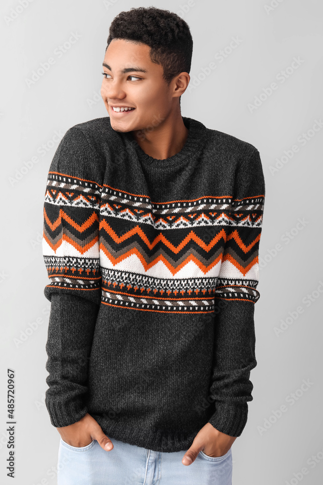 Handsome African-American guy in knitted sweater on light background