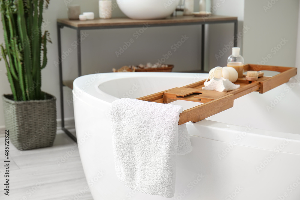 Wooden tray with accessories and candle on bathtub in room