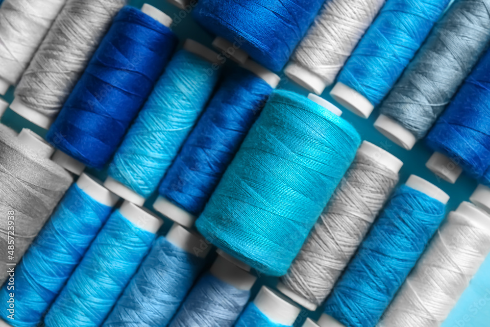 Closeup view of spools with grey and blue sewing threads as background