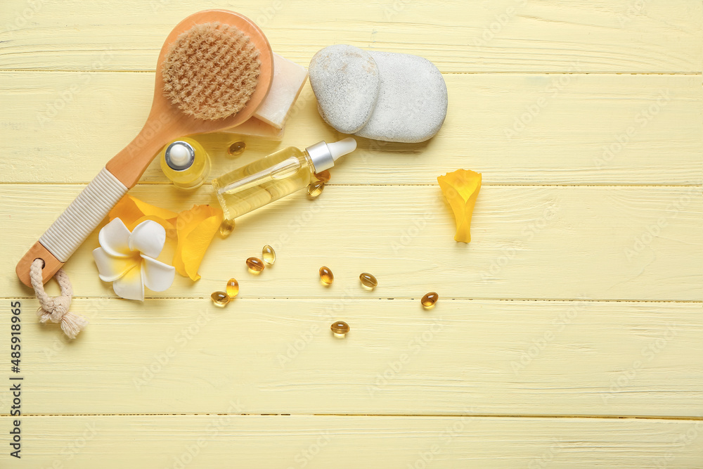 Composition with bottles of essential oil, pills, massage brush and soap on color wooden background