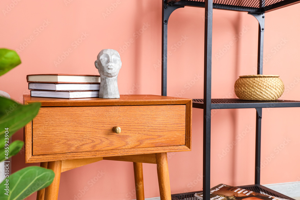 Wooden table with books and decor near pink wall